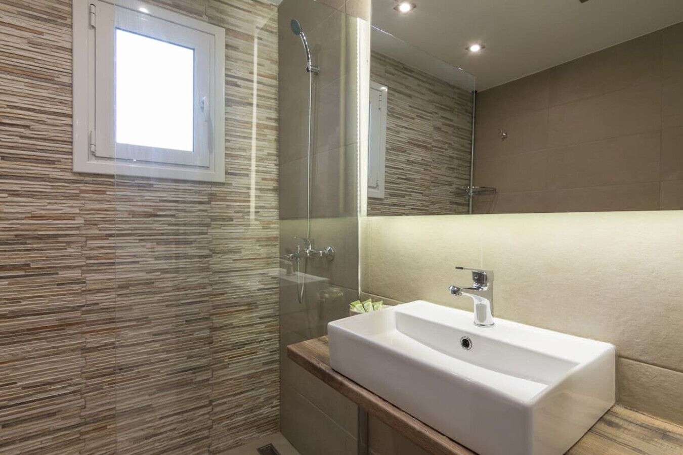 Une salle de bain moderne avec une douche à l’italienne en verre, un lavabo blanc et un grand miroir.