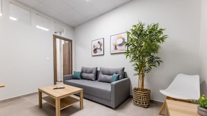 Un salon moderne avec un canapé gris, une table basse en bois, une grande plante en pot et une chaise blanche.
