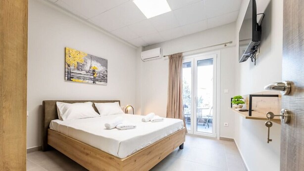 Une chambre moderne avec un lit en bois, un tableau au mur et une porte-fenêtre coulissante donnant sur le balcon.