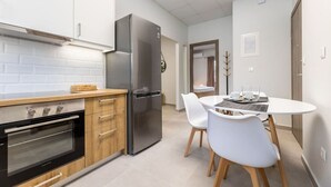 Une cuisine moderne dotée d’un four encastré, d’un réfrigérateur en acier inoxydable et d’un coin repas avec une table ronde et des chaises blanches.