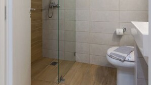 A modern bathroom with a glass shower enclosure, a wooden floor, and a white toilet.