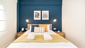 A neatly made bed with two towels, a blue headboard, and two framed artworks above it.