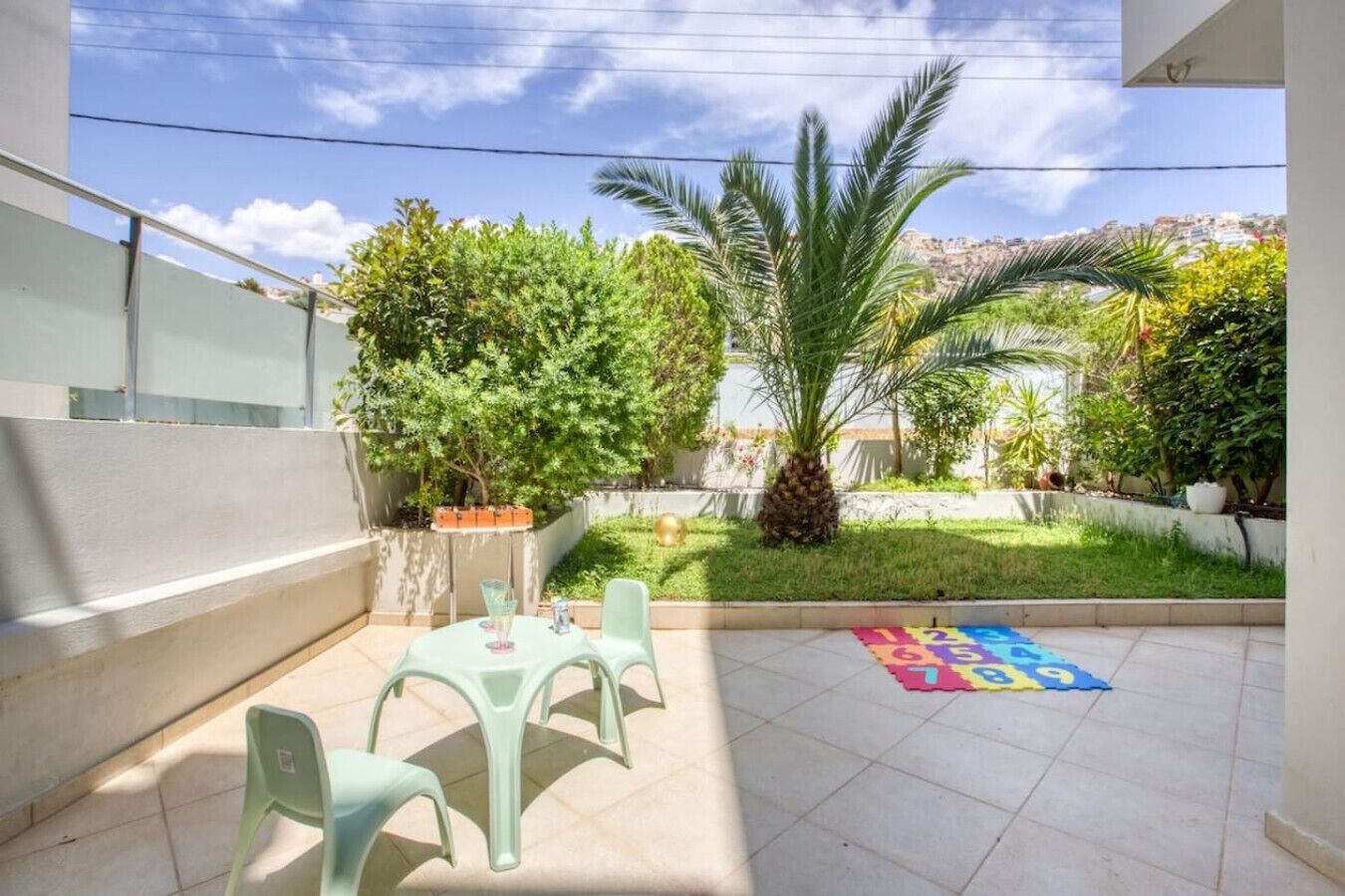 A patio area with a table and chairs, a palm tree, and a colorful play mat.