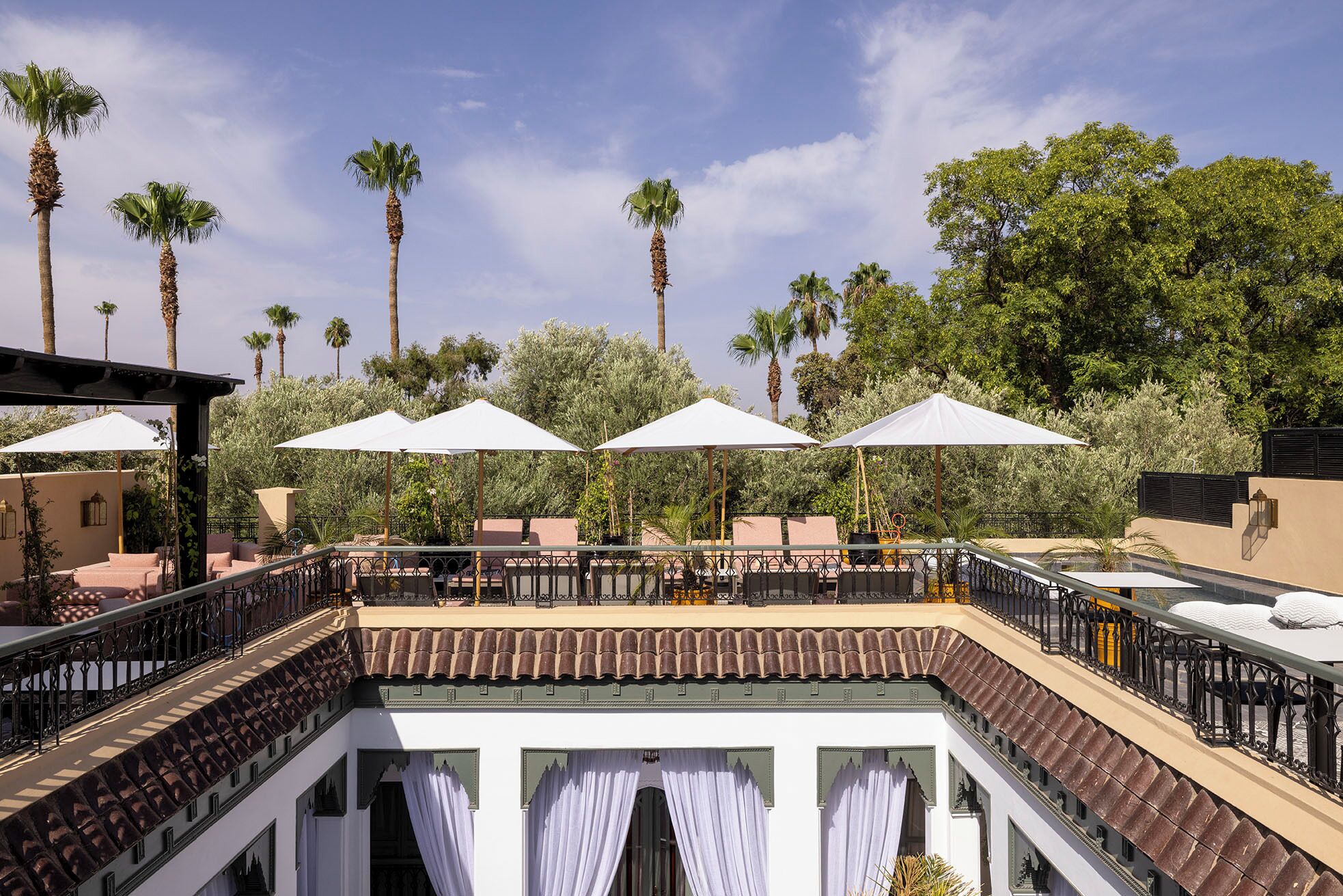 A rooftop terrace with outdoor seating, palm trees, and a pool.