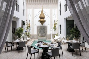 Un espace repas avec des tables et des chaises rondes, une fontaine décorative et un mur orné d’un motif en arrière-plan.