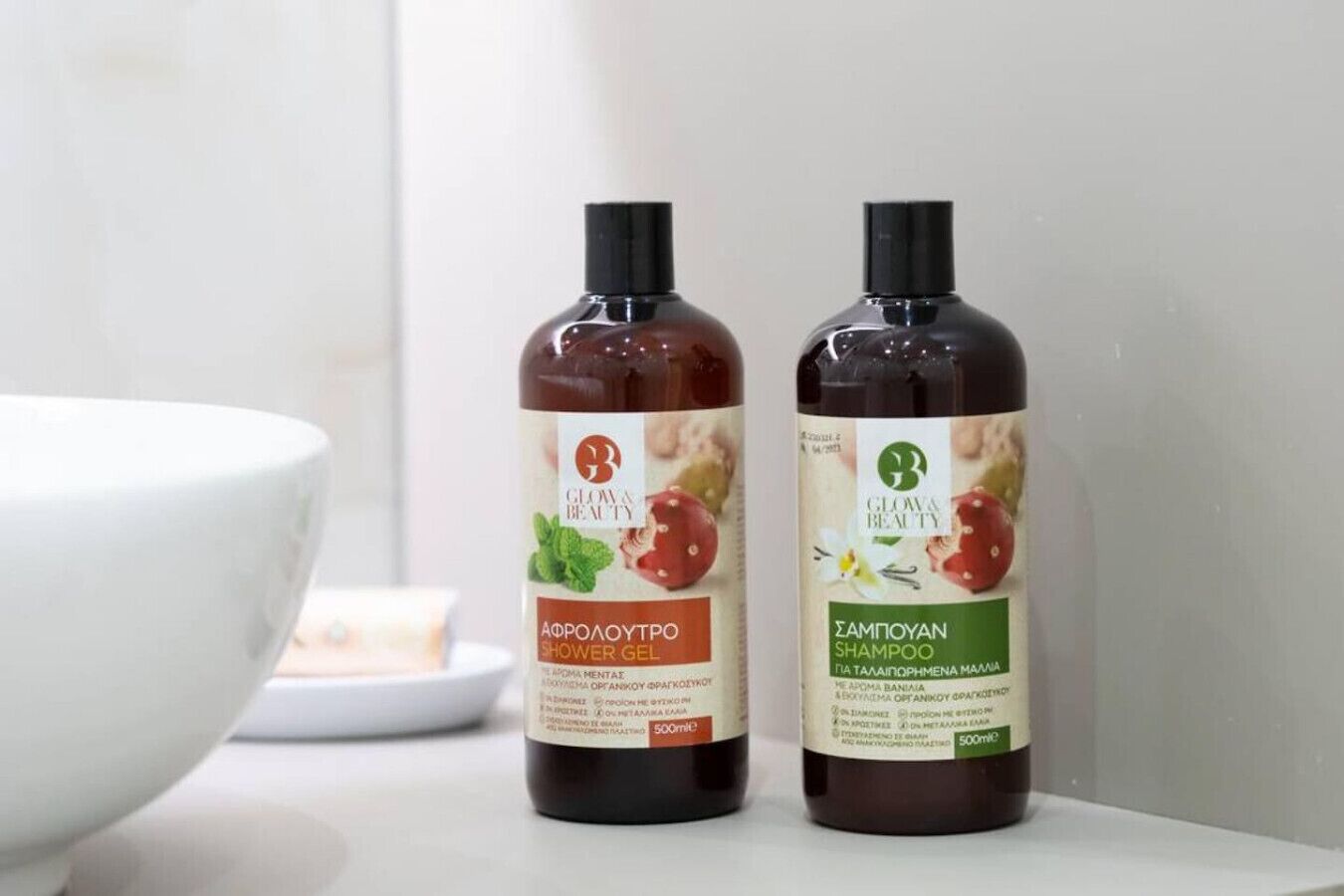 Two bottles of shower gel and shampoo on a white surface with a white bowl in the background.