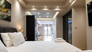 A modern hotel room with a large bed, a desk, and a view of the dining area.