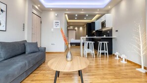 A modern living room with a grey sofa, a round wooden coffee table, and a kitchen area with a bar and stools.