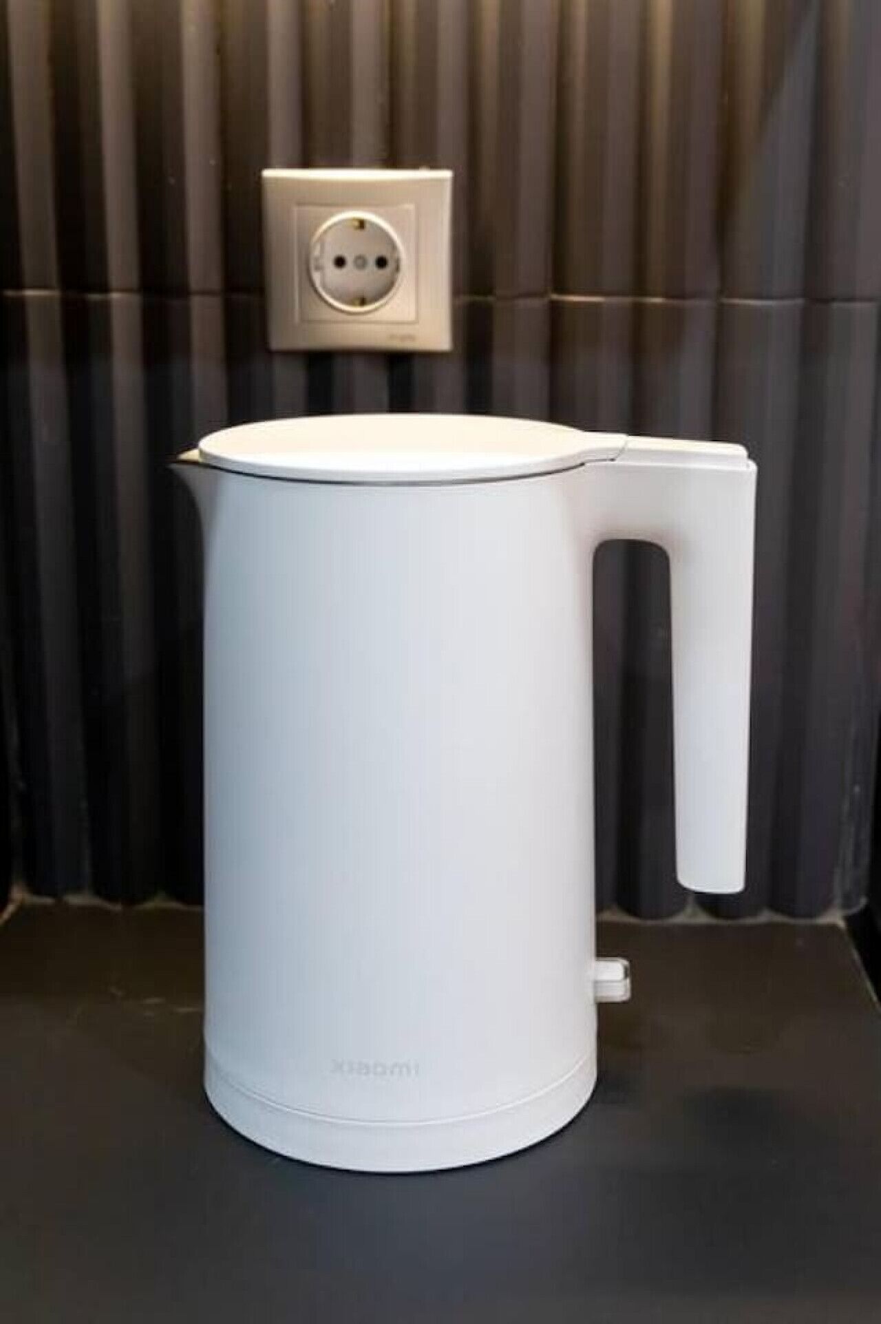 A white electric kettle with a handle on a black countertop.