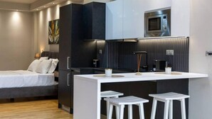 A modern hotel room with a bed, a kitchenette, and a small bar area with stools.