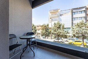A balcony with a table and chairs, overlooking a street with cars and buildings.