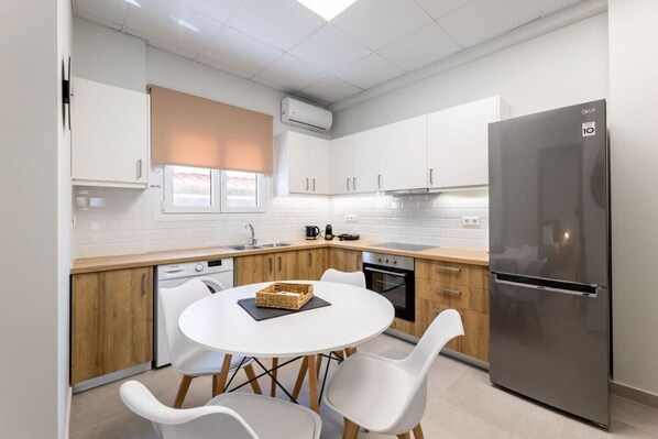 A modern kitchen with white cabinets, a stainless steel refrigerator, a dishwasher, and a round dining table with white chairs.