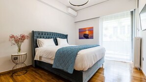A modern bedroom with a large bed, a bedside table with a vase of flowers, a painting on the wall, and a large window. - Luxury flat at archaeological museum (Athina)