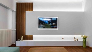 A modern interior with a large flat-screen TV mounted on a white wall, a wooden bench, and a small table with decorative items. - Luxury flat at archaeological museum (Athina)