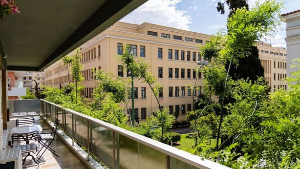 A balcony with outdoor furniture, a view of a building with multiple windows, and surrounding greenery. - Luxury flat at archaeological museum (Athina)