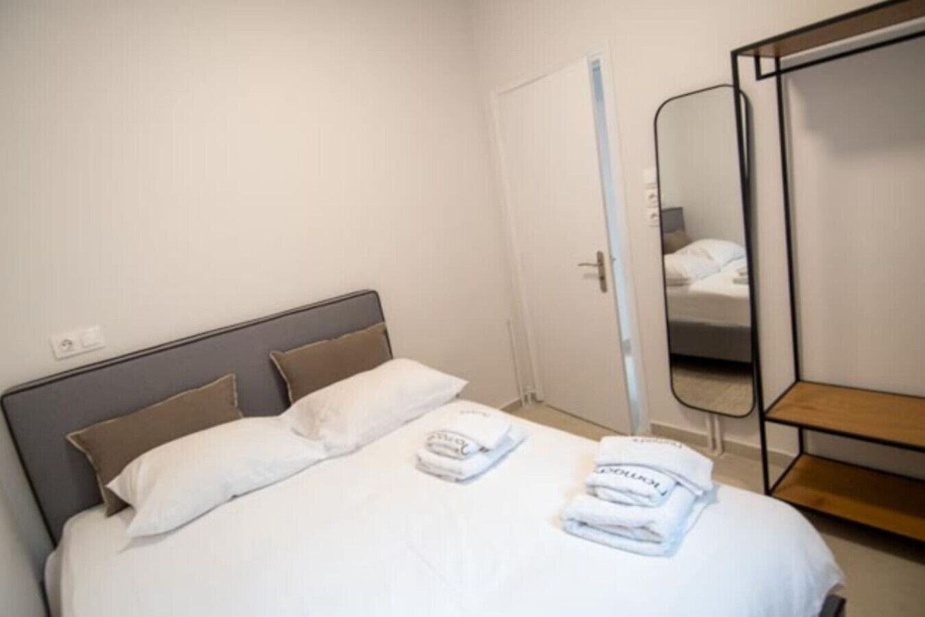 A hotel room with a bed, a bedside table, a mirror, and a door.