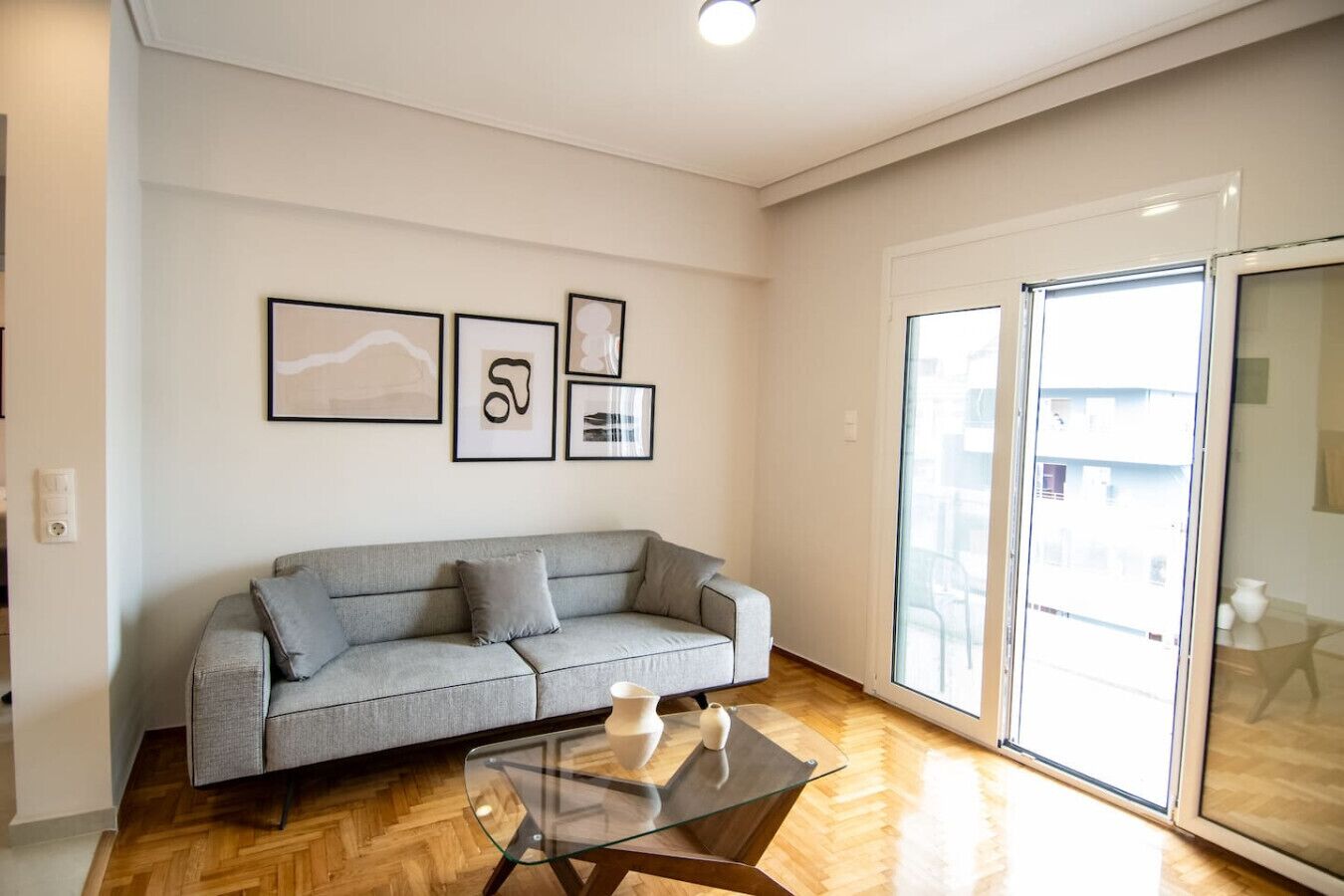 Una sala de estar moderna con un sofá gris, una mesa de centro de vidrio y obras de arte enmarcadas en la pared.
