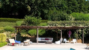 A pool area with a pergola, lounge chairs, and a sofa.