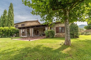 Une maison en pierre dotée d’un patio couvert et d’un espace extérieur aménagé pour s’asseoir.