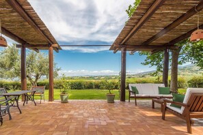 Une terrasse couverte avec un sol en briques, des meubles d’extérieur et des plantes en pot.