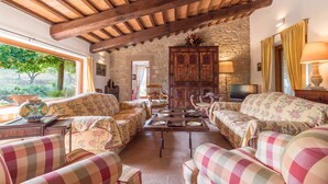 A cozy living room with a stone wall, wooden ceiling beams, and floral-patterned furniture.