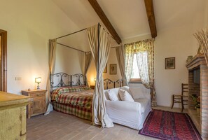 Une chambre à coucher avec un lit à baldaquin, un canapé blanc, un tapis à motifs rouges et une cheminée.