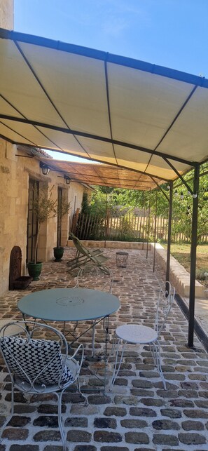 Eine überdachte Terrasse mit Steinböden, Metallstühlen und einem Tisch.