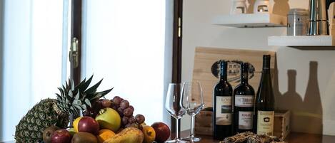 A fruit bowl with various fruits and two wine glasses on a wooden table.