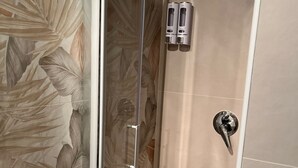 Une douche avec une porte en verre, un panneau de commande et un mur orné d’un motif de feuilles.