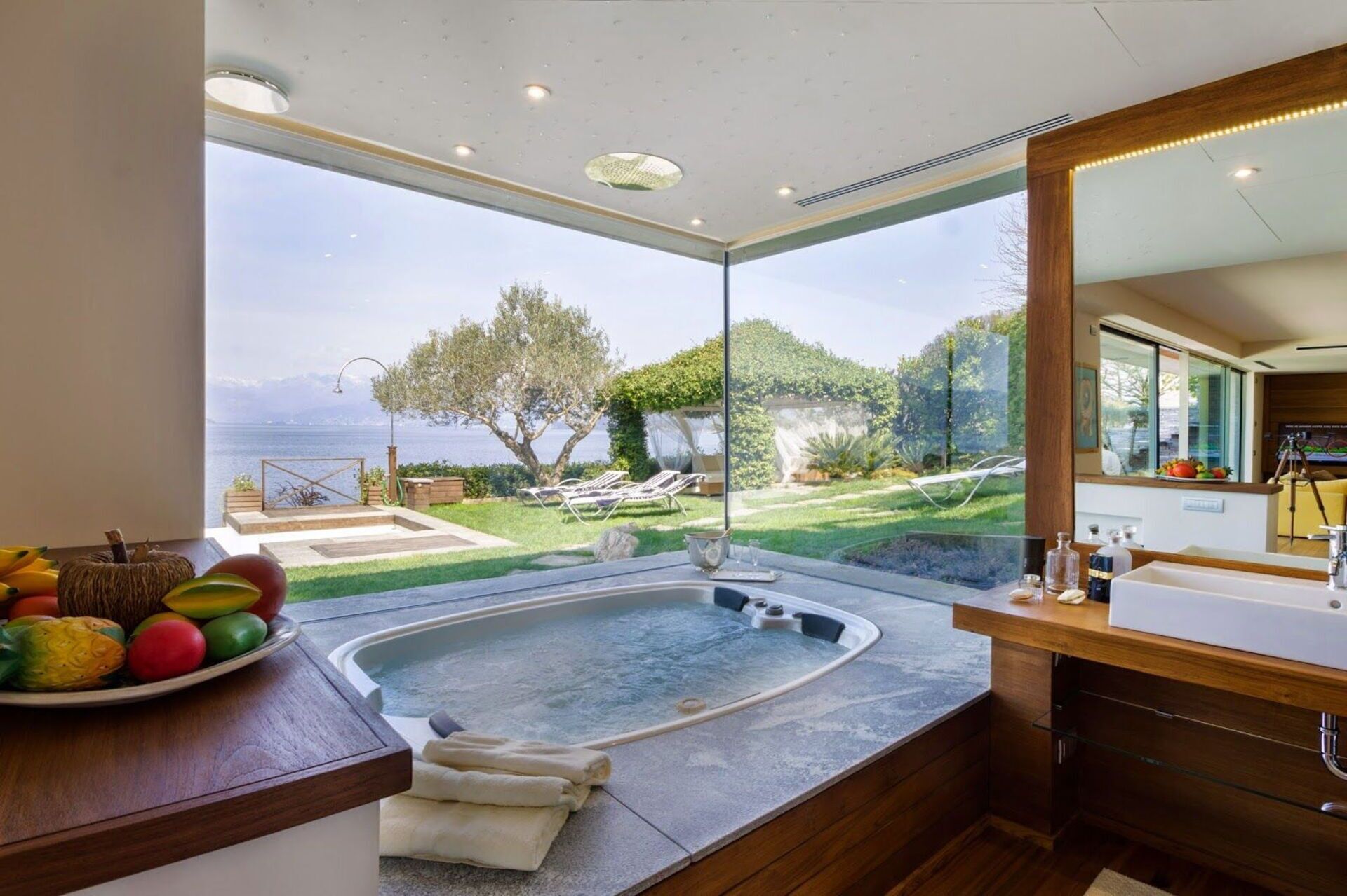 A modern bathroom with a hot tub, large windows, and a view of the sea.