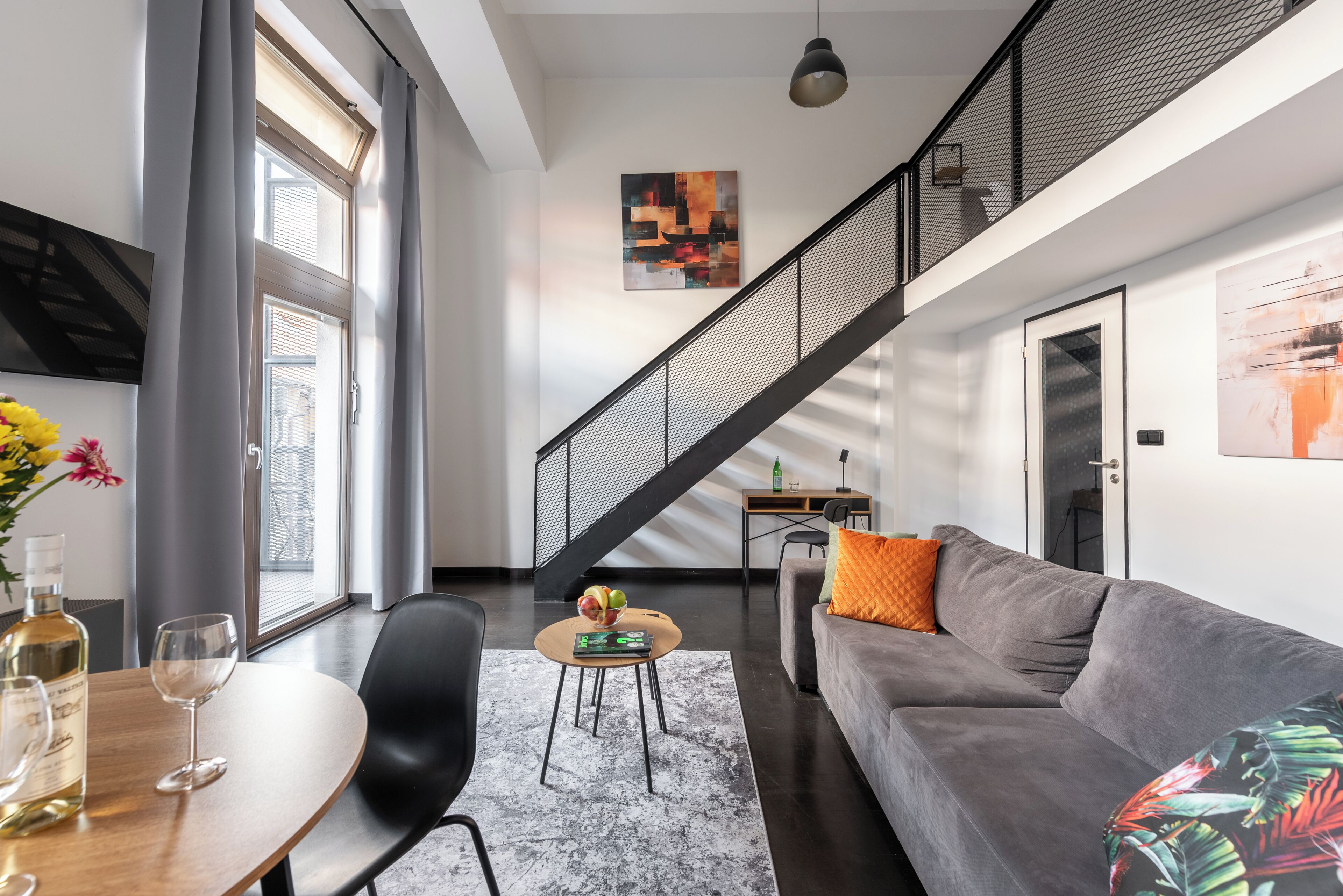 Una sala de estar moderna con un sofá, una mesa de comedor con sillas, una mesa auxiliar y una escalera.