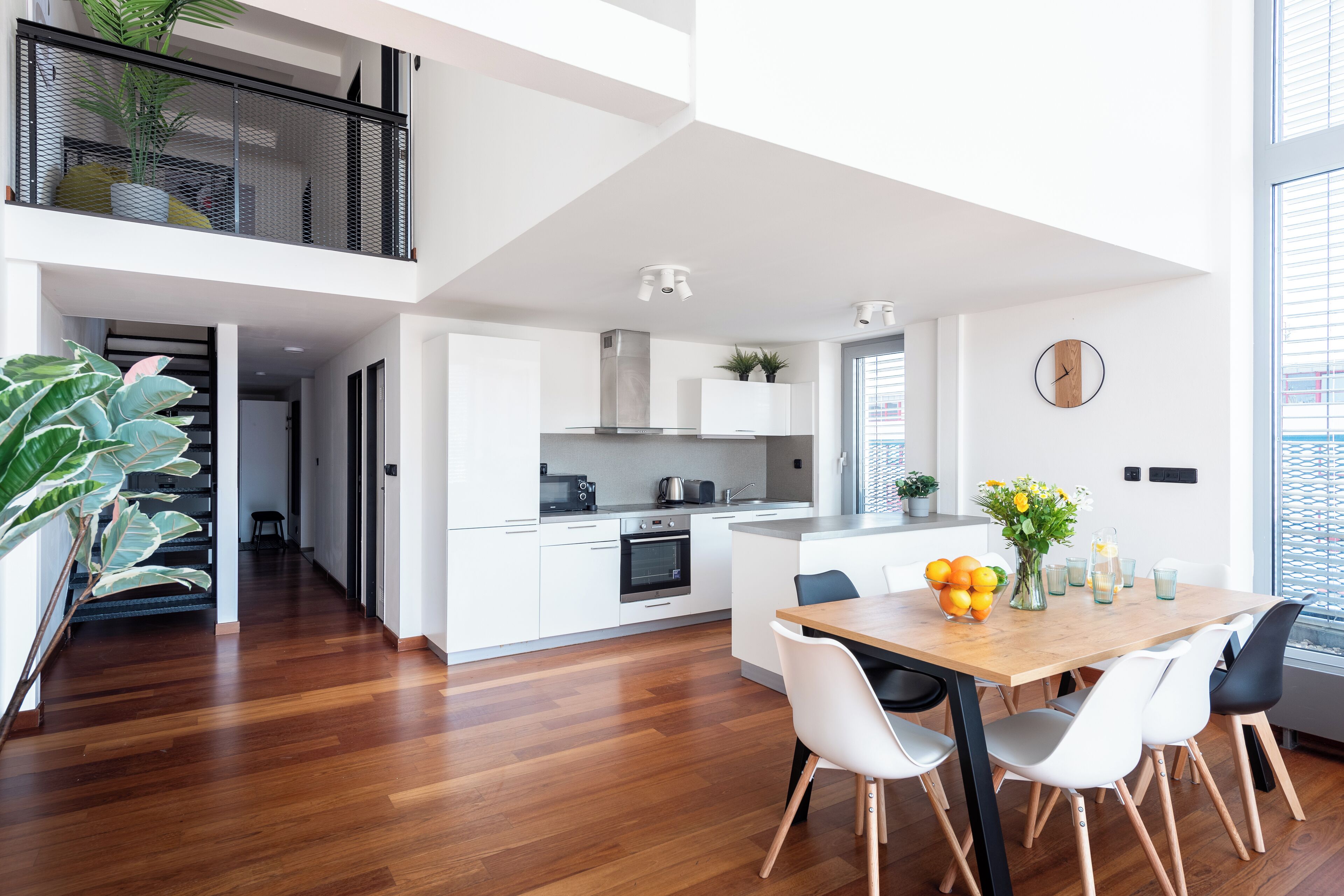 A modern kitchen with white cabinets, a wooden dining table, and a large window.