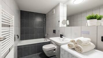 Een moderne badkamer met een bad, toilet en wastafel. Handdoeken liggen op de wastafel gestapeld en er staat een potplant op het aanrecht.