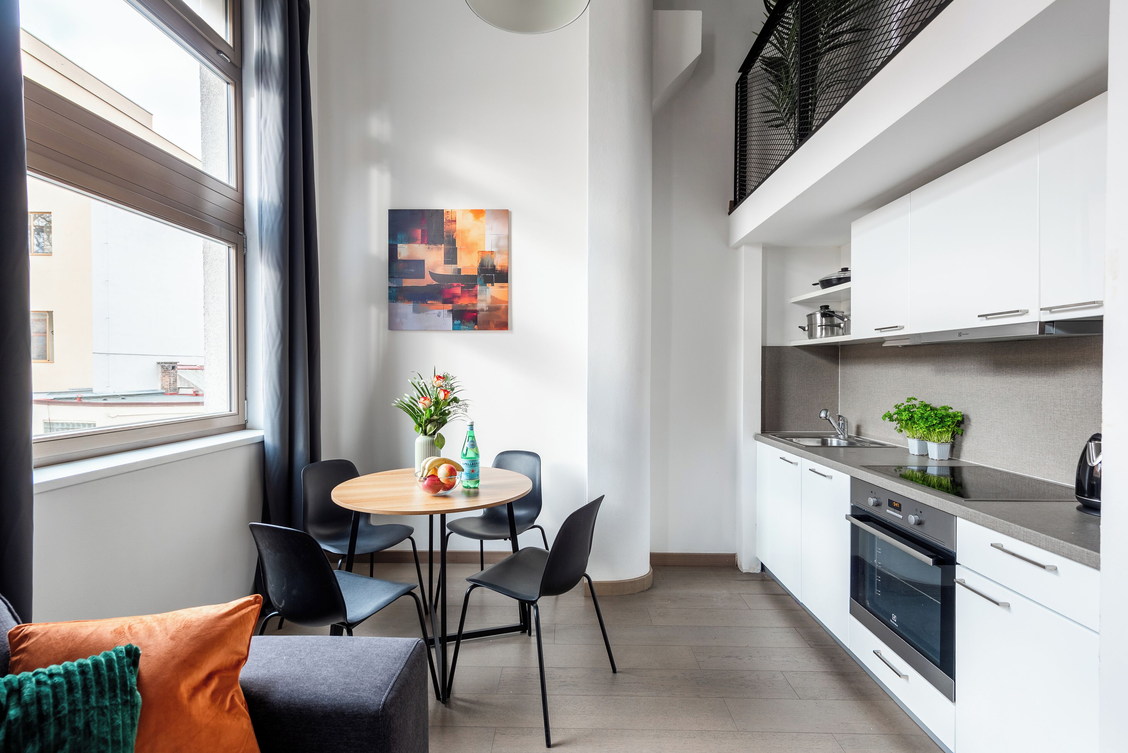 Et moderne køkken med hvide skabe, indbygget ovn samt spiseplads med et rundt bord og stole.