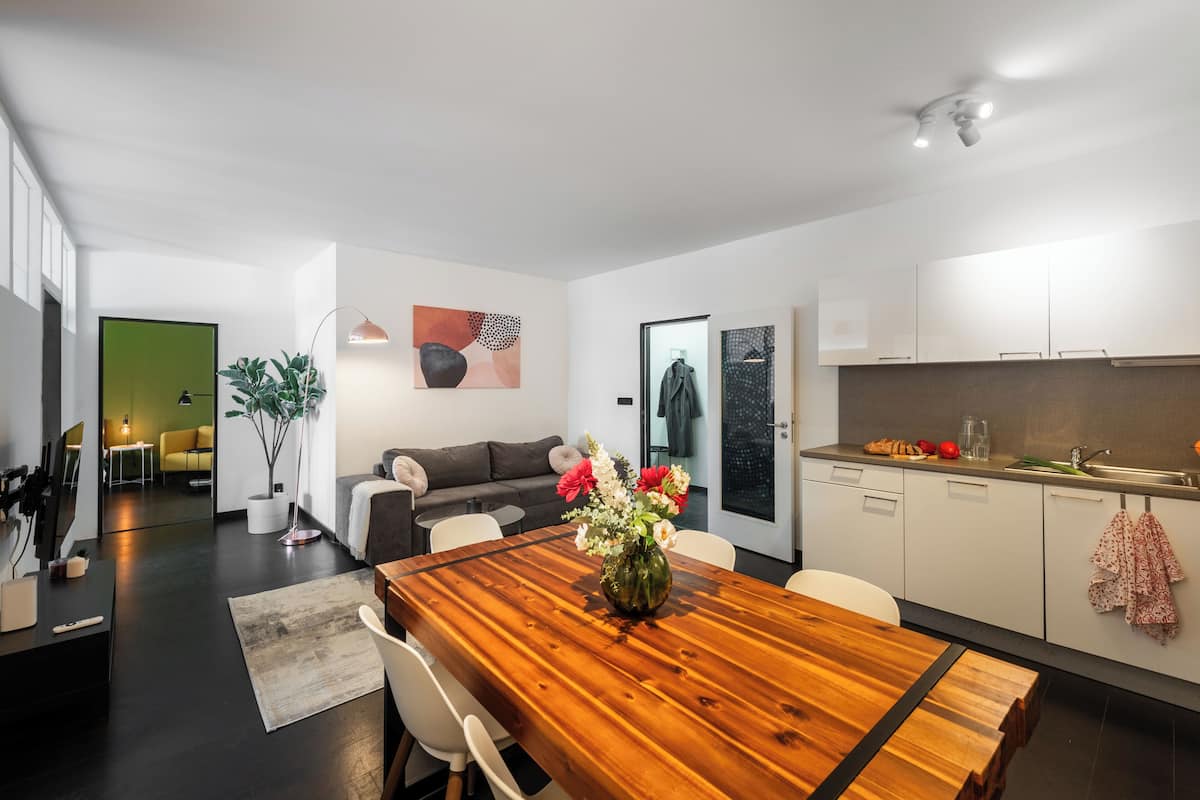 Een moderne woonruimte met een houten eettafel, een bank, een keukenhoek en een groot raam.