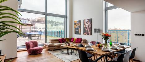 Ein großzügiger Wohnbereich mit einem großen Fenster, einem Sofa, einem Esstisch mit Stühlen und einem roten Sessel.