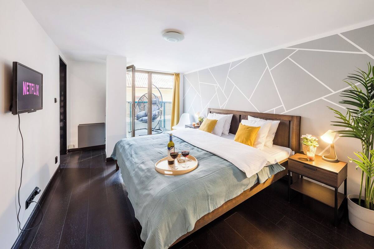 Een moderne hotelkamer met een groot bed, een nachtkastje met lamp, een potplant en een aan de muur bevestigde televisie waarop het Netflix-logo staat.