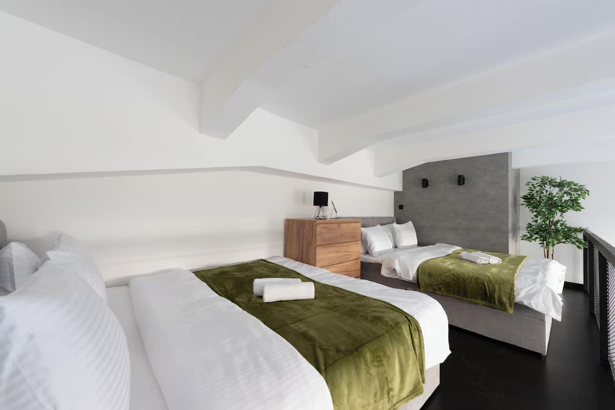 Een moderne hotelkamer met twee bedden, een houten nachtkastje, een grijze hoofdbord en een pot met een plant.