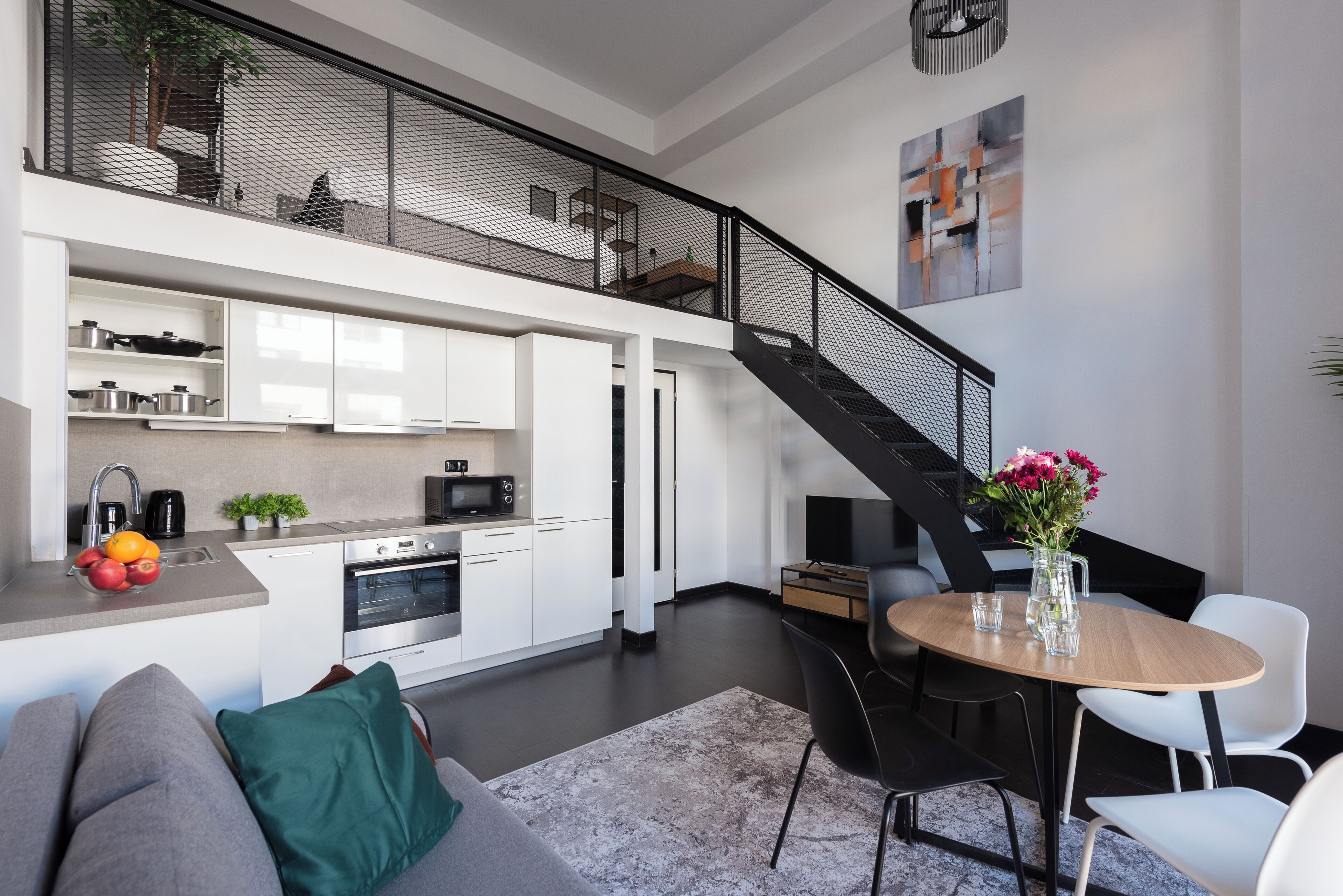 Een moderne keuken met witte kastjes, een magnetron en een koffiezetapparaat. Er is een eethoek met een ronde tafel en stoelen.