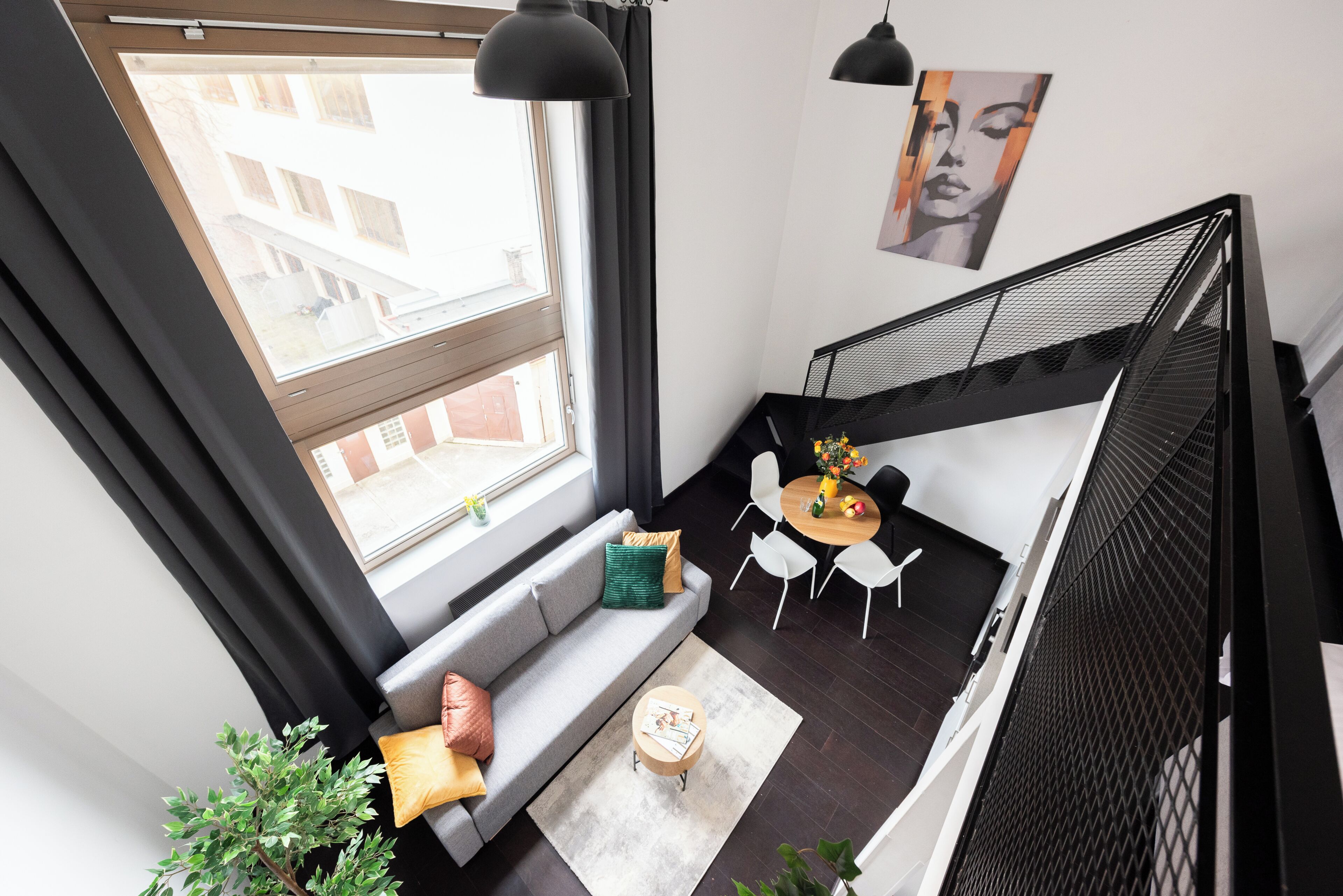 Een modern loft appartement met een groot raam, een bank, een klein rond tafeltje en een trap.