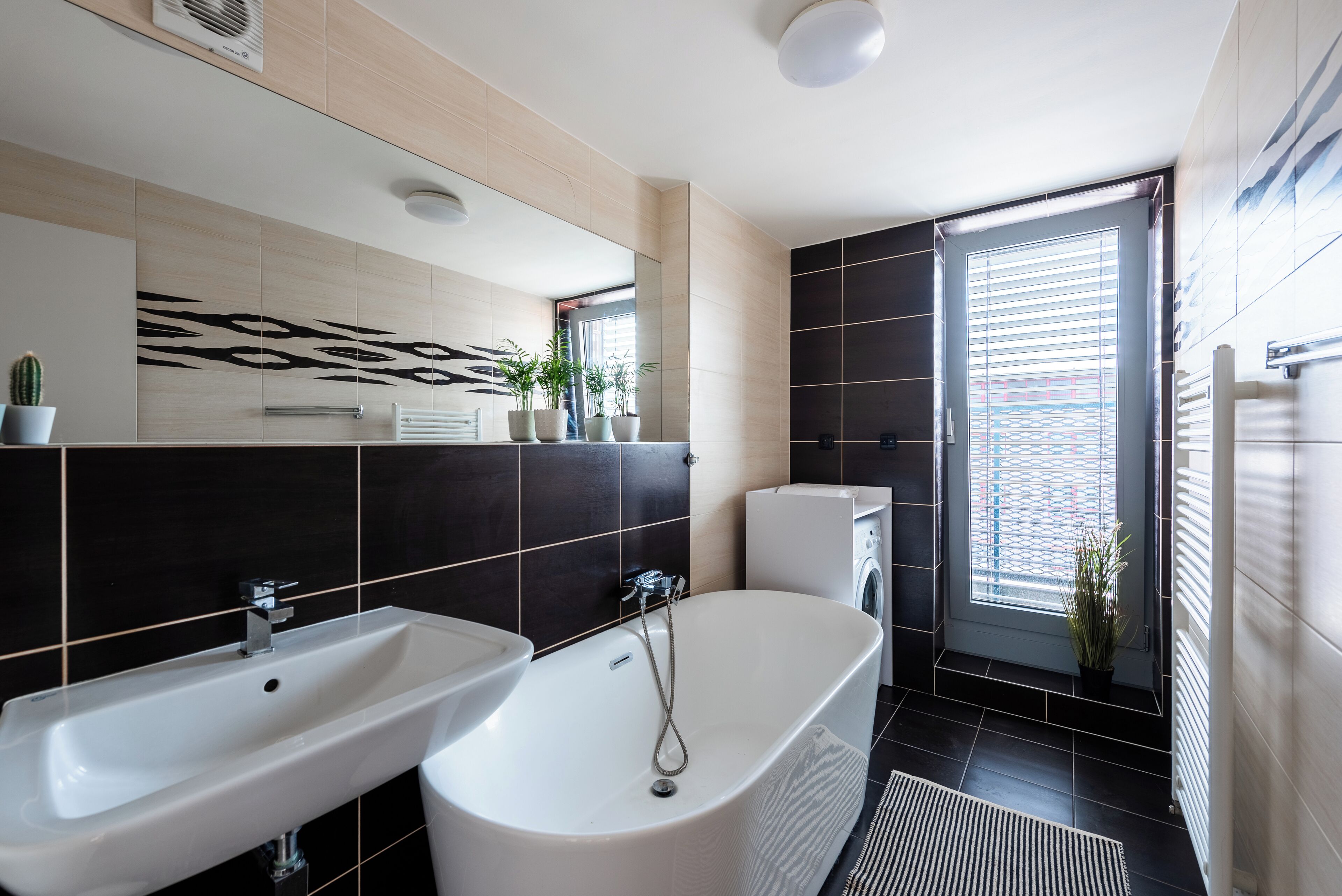 Een moderne badkamer met een vrijstaand bad, twee wastafels en een grote spiegel.