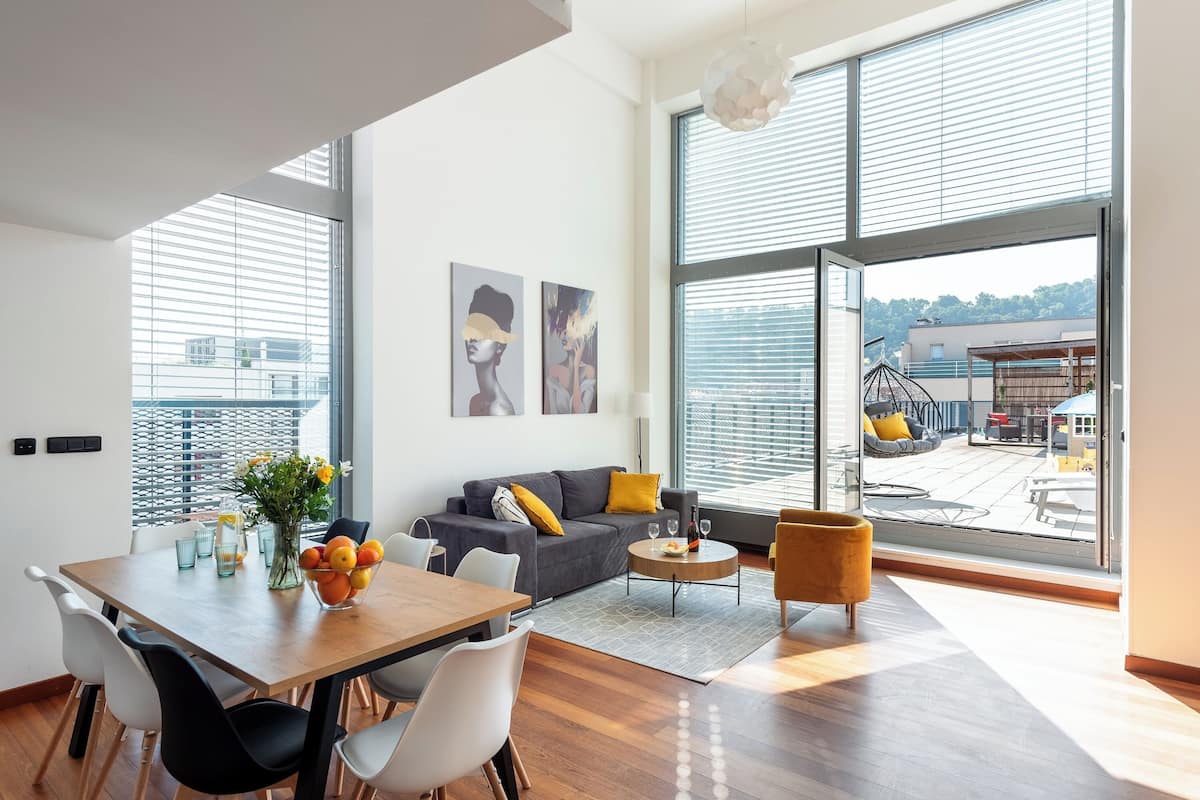 Een moderne woonkamer met een eethoek, grote ramen en uitzicht op buiten.