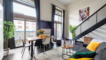 A modern living room with a sofa, coffee table, and dining area with chairs. There is a staircase with a railing and a plant on the floor.