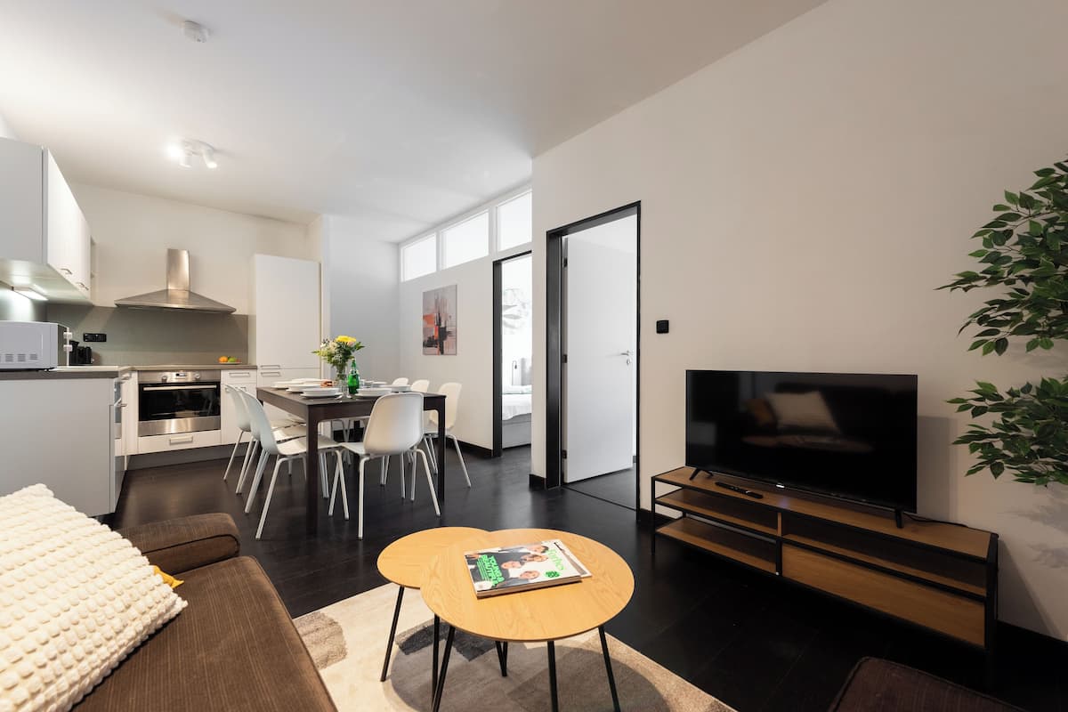 Een moderne woonkamer met een bank, een salontafel, een televisie en een eethoek met stoelen en een tafel.