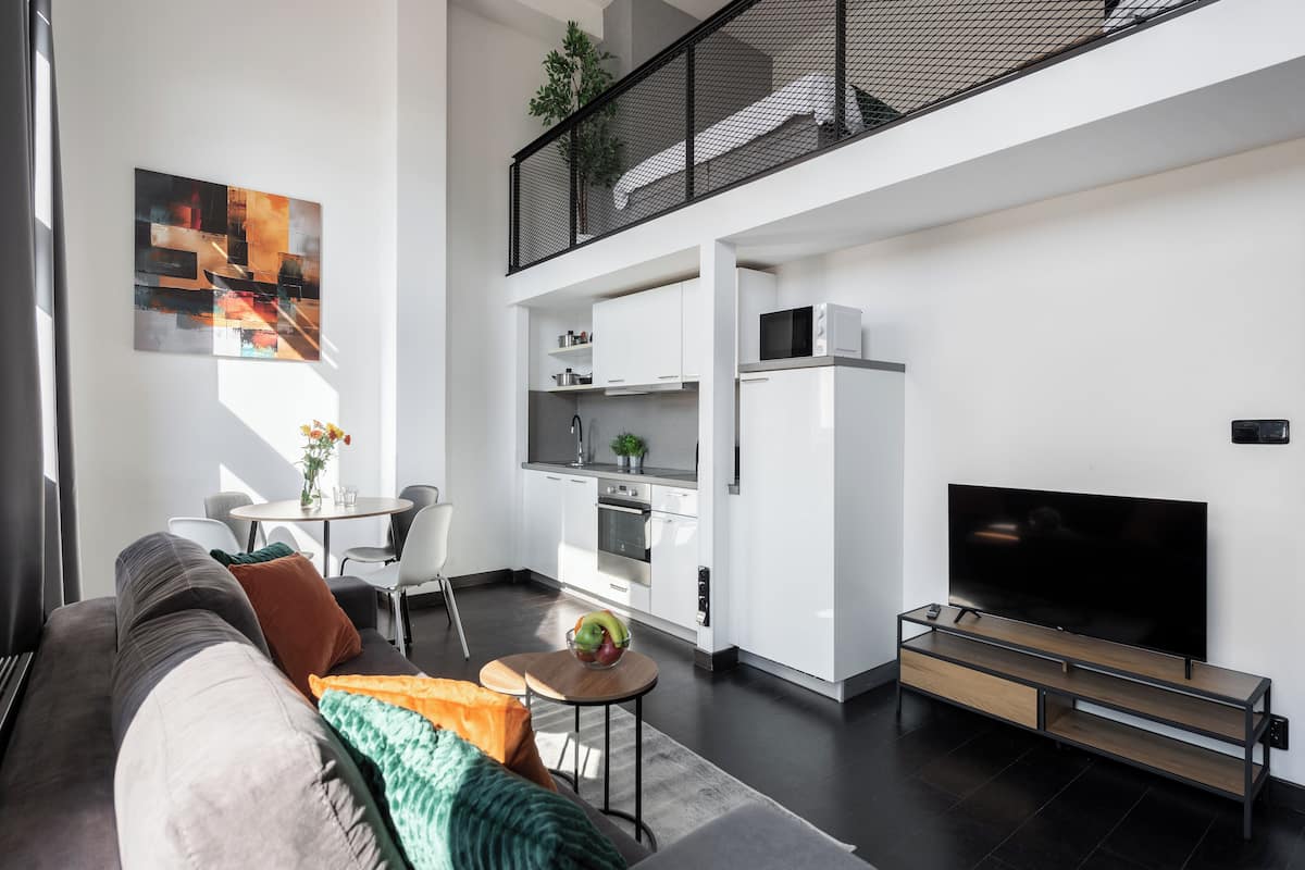 Een moderne woonkamer met een bank, een eettafel en een keukenhoek met een televisie en magnetron.