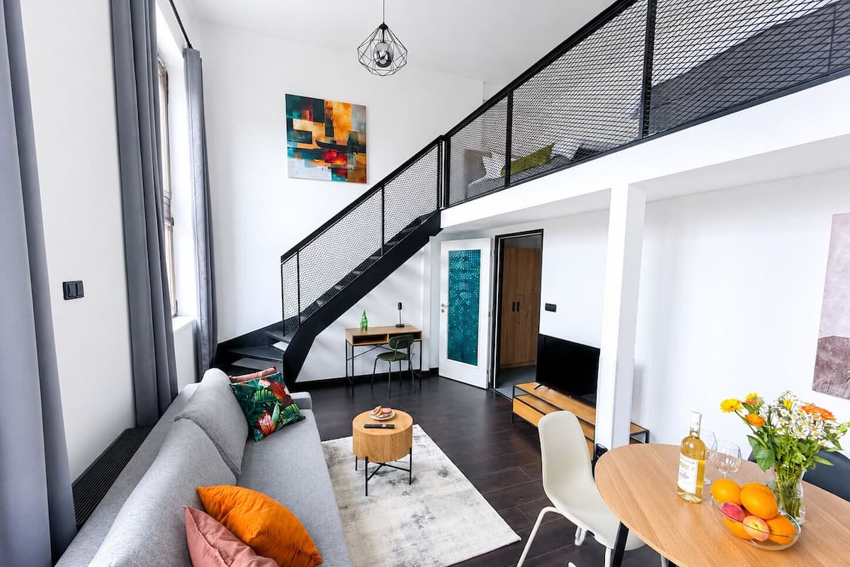 Een moderne woonruimte met een grijze bank, een eettafel met fruit, een trap en een kunstwerk aan de muur.