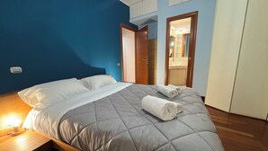 A neatly made bed with pillows and rolled towels, a bedside table with a lamp, and a bathroom visible through an open door. - Charm Apartment Rome Gemini - Relax Jacuzzi (Roma)