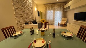 A dining area with a glass table, plates, cutlery, and a bottle of champagne. There is a sofa and a TV in the background. - Charm Apartment Rome Gemini - Relax Jacuzzi (Roma)