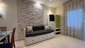 A modern living room with a stone wall, a sofa with storage drawers, a dining table with chairs, and a wardrobe. - Charm Apartment Rome Gemini - Relax Jacuzzi (Roma)