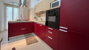 A modern kitchen with red cabinets, a stainless steel range hood, a microwave, and a built-in oven. - Charm Apartment Rome Gemini - Relax Jacuzzi (Roma)